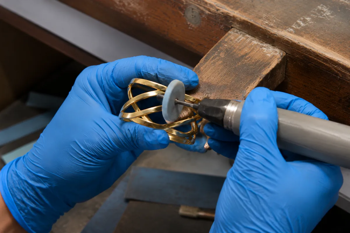 Jewelry worker polishing a gold-tone bracelet at a worn wooden production workbench